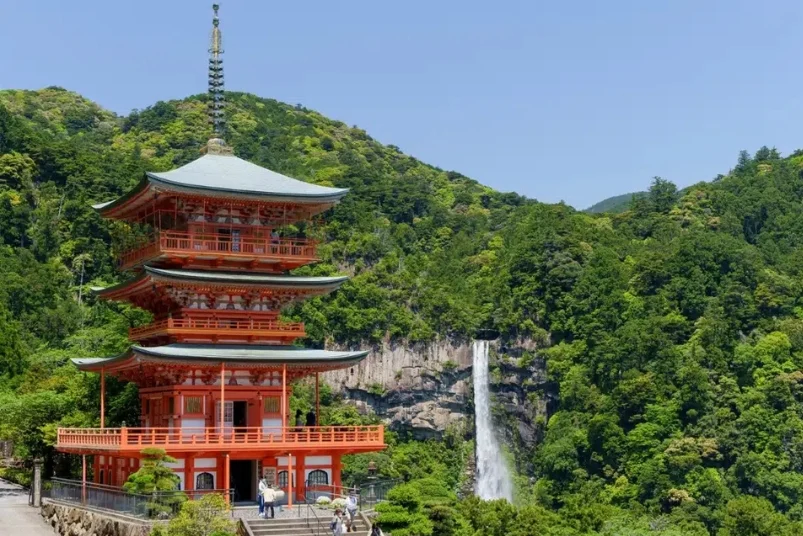 A vermillion three-story pagoda with Nachi Falls and a lush green forest.