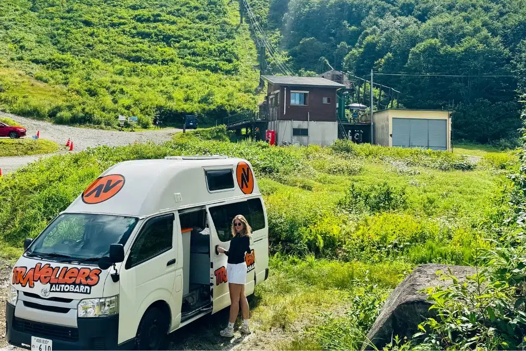 Traveler standing by a Travellers Autobarn campervan near mountain slopes in Hakuba during summer