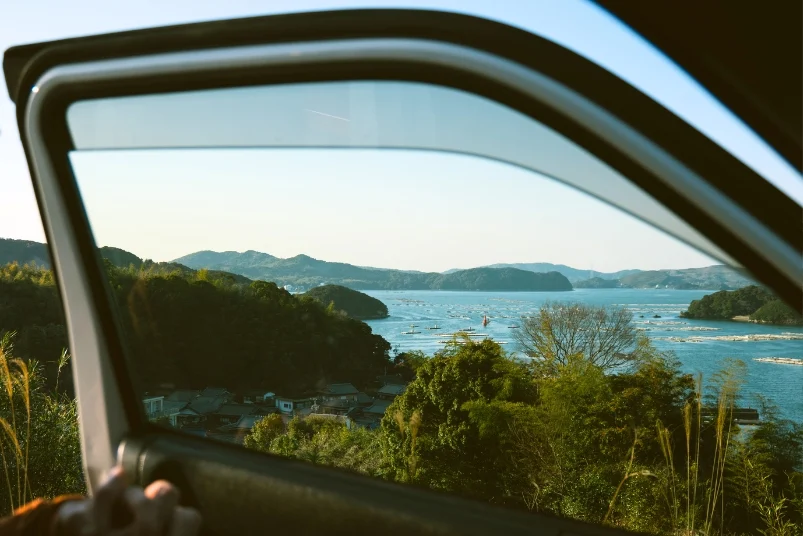 A scenic view of a calm ria coast and fishing village in Ise-Shima, seen through the window of a campervan.