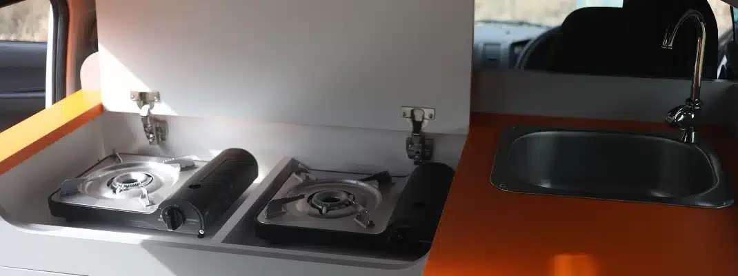 Compact campervan kitchenette featuring a stainless steel sink with a faucet and two portable gas stoves.