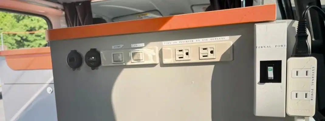 Internal power supply control panel inside a campervan with AC power outlets, USB charging ports, and appliance switches.