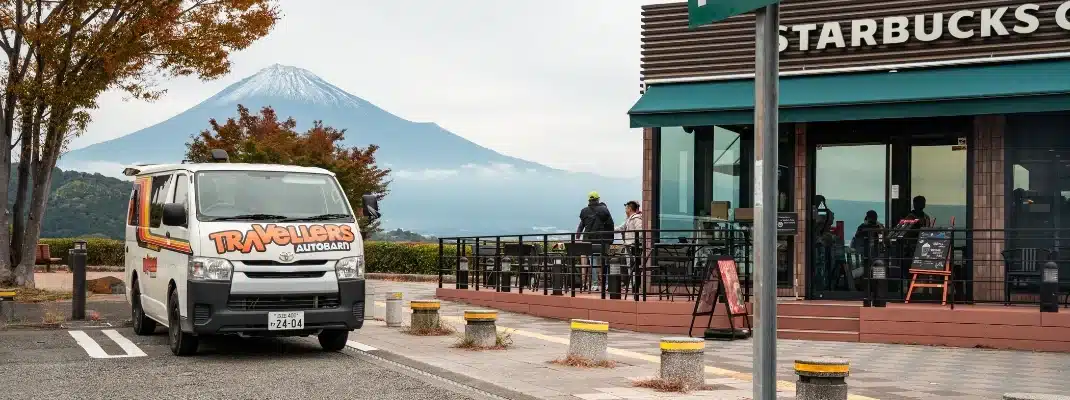 A Travellers Autobarn campervan parked in front of a Starbucks with Mount Fuji in the background