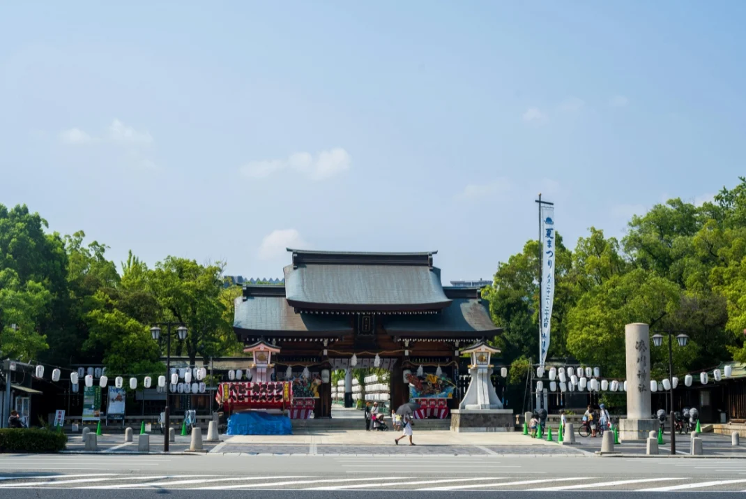 Entrance gate of a traditional Japanese shrine decorated with paper lanterns and festival banners under a clear blue sky.