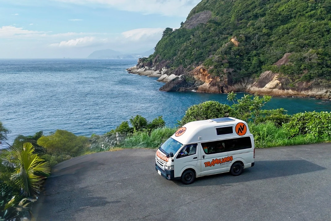 A Travellers Autobarn campervan parked on a scenic coastal viewpoint overlooking dramatic cliffs and deep blue ocean waters along the Izu Peninsula.