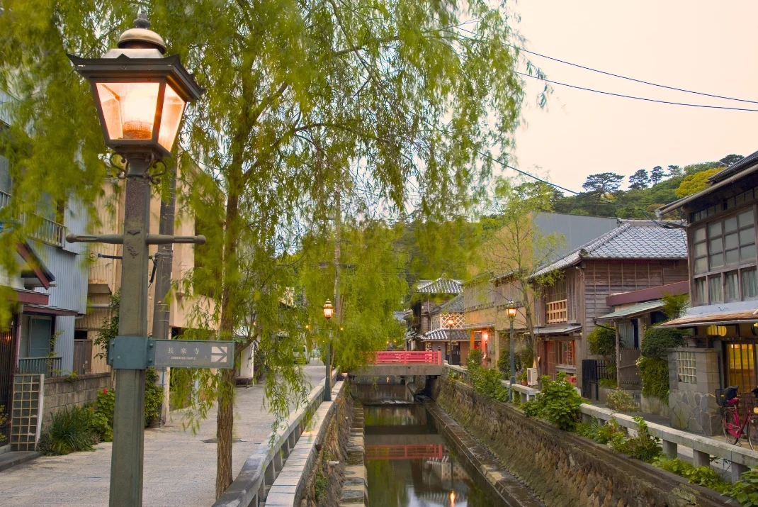 A peaceful canal street on Perry Road in Shimoda, lined with traditional historic buildings, weeping willow trees, and warm street lamps.